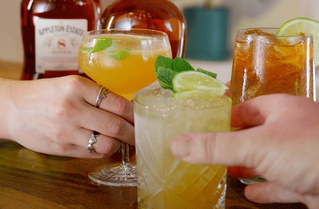 Hands reaching for 3 cocktails made with Appleton Estate rum