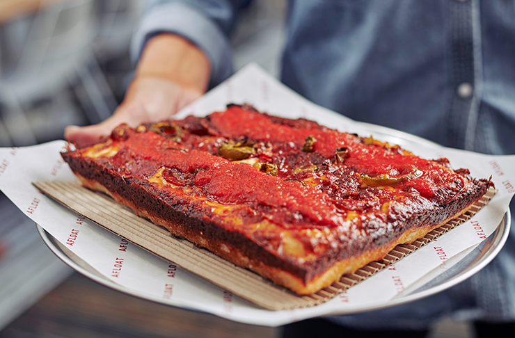 A deep dish pizza on a round plate covered in red sauce.