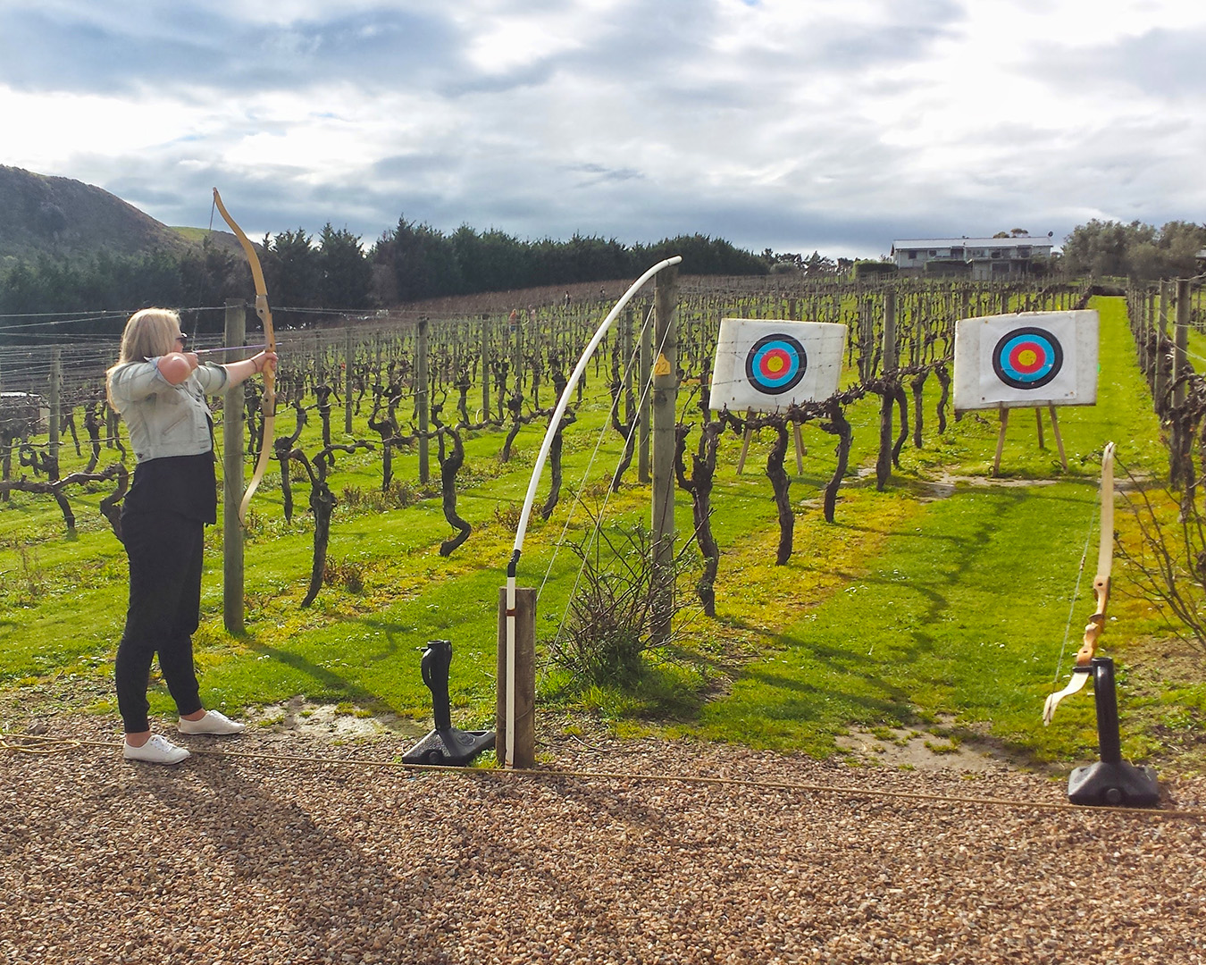 A girl takes aim with a bow and arrow at archery amongst the vines.
