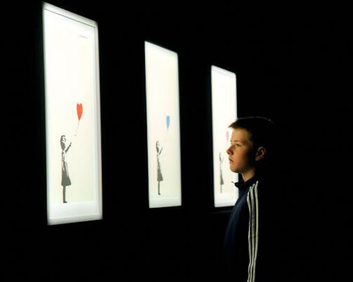 A young boy looks at three illuminated installations of Banksy's 'Girl with Balloon'.