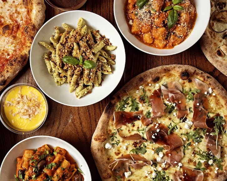 A table full of pizza and pasta dishes. 