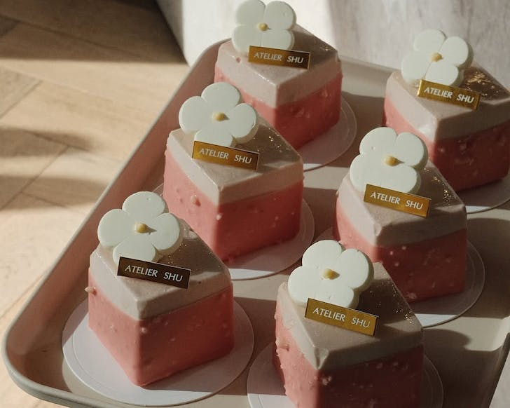 A ceramic tray of six petite strawberry Basque cheesecakes topped with a flower and a gold sign that says Atelier Shu.