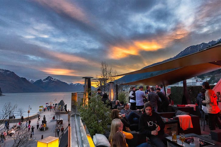 People frequent a beautiful rooftop bar in front of a stormy Queenstown sky.