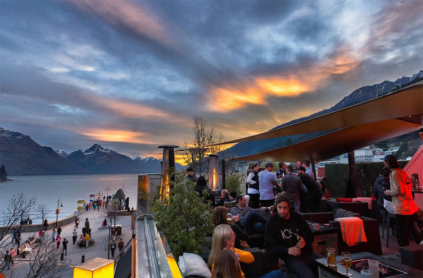 People frequent a beautiful rooftop bar in front of a stormy Queenstown sky.