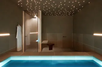 Render of AURA Spa & Bathhouse's float therapy room featuring a glowing float pool, star-like ceiling lights, walk-in shower and calming minimalist interiors.