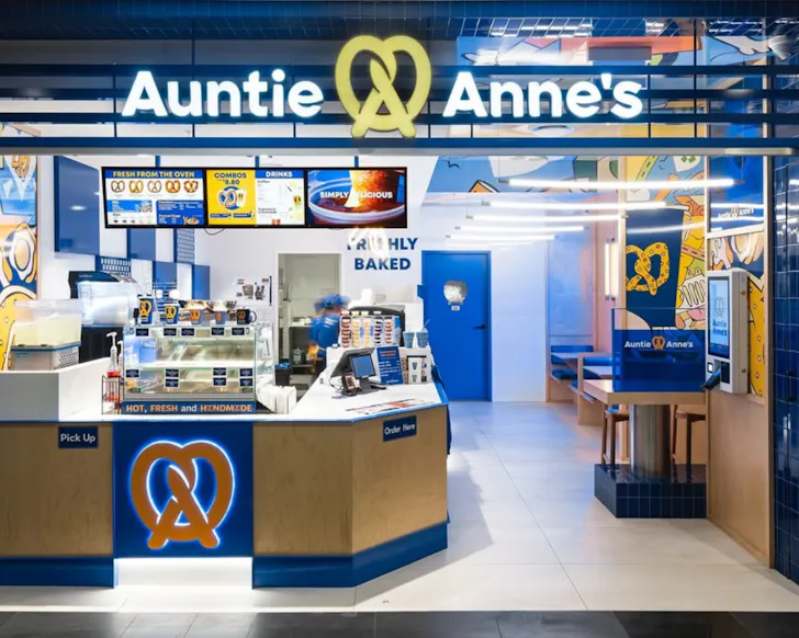 Exterior of Auntie Anne's pretzel store in Brisbane, with illuminated signage, bright blue interiors and the front counter visible through the open shopfront.