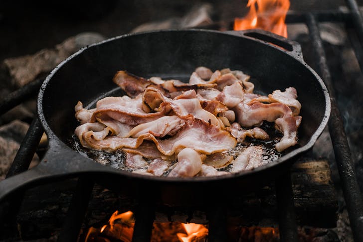 a pan of sizzling bacon over coals