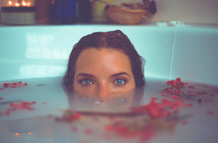 A woman sits in an almond milk bath with only her eyes showing above the waterline.