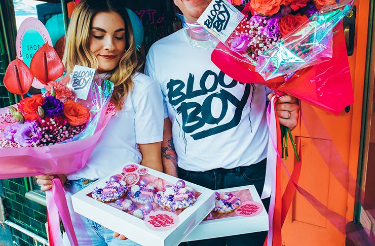 Two people holding colourful flowers and cakes.