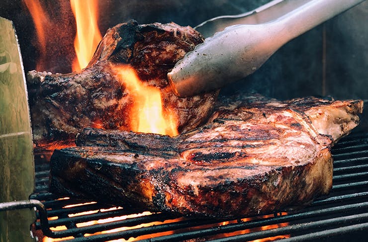 Two thick pieces of steak grilling on a flaming barbecue.
