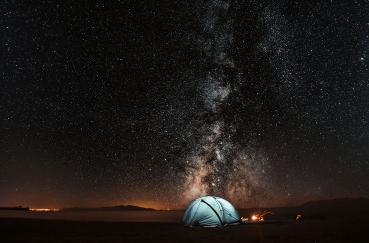 A tent pitched on a beach with the Milky Way and starry night sky in the background. 