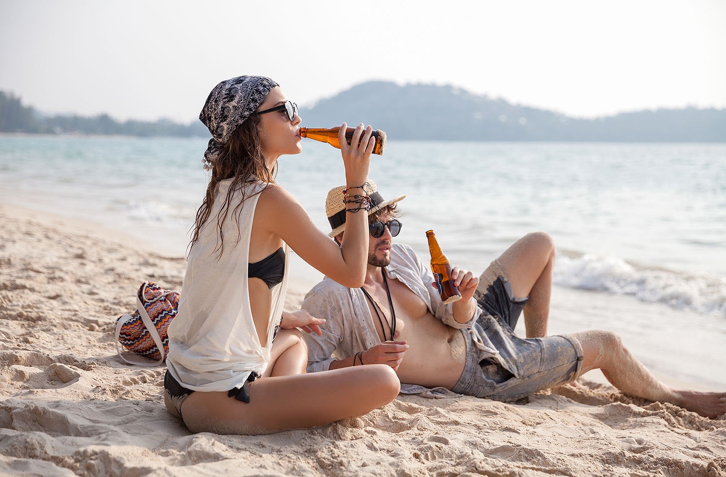 A couple sit on the beach drinking beers