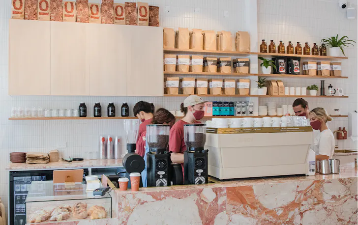 the front counter of a cafe, with a coffee machine and staff
