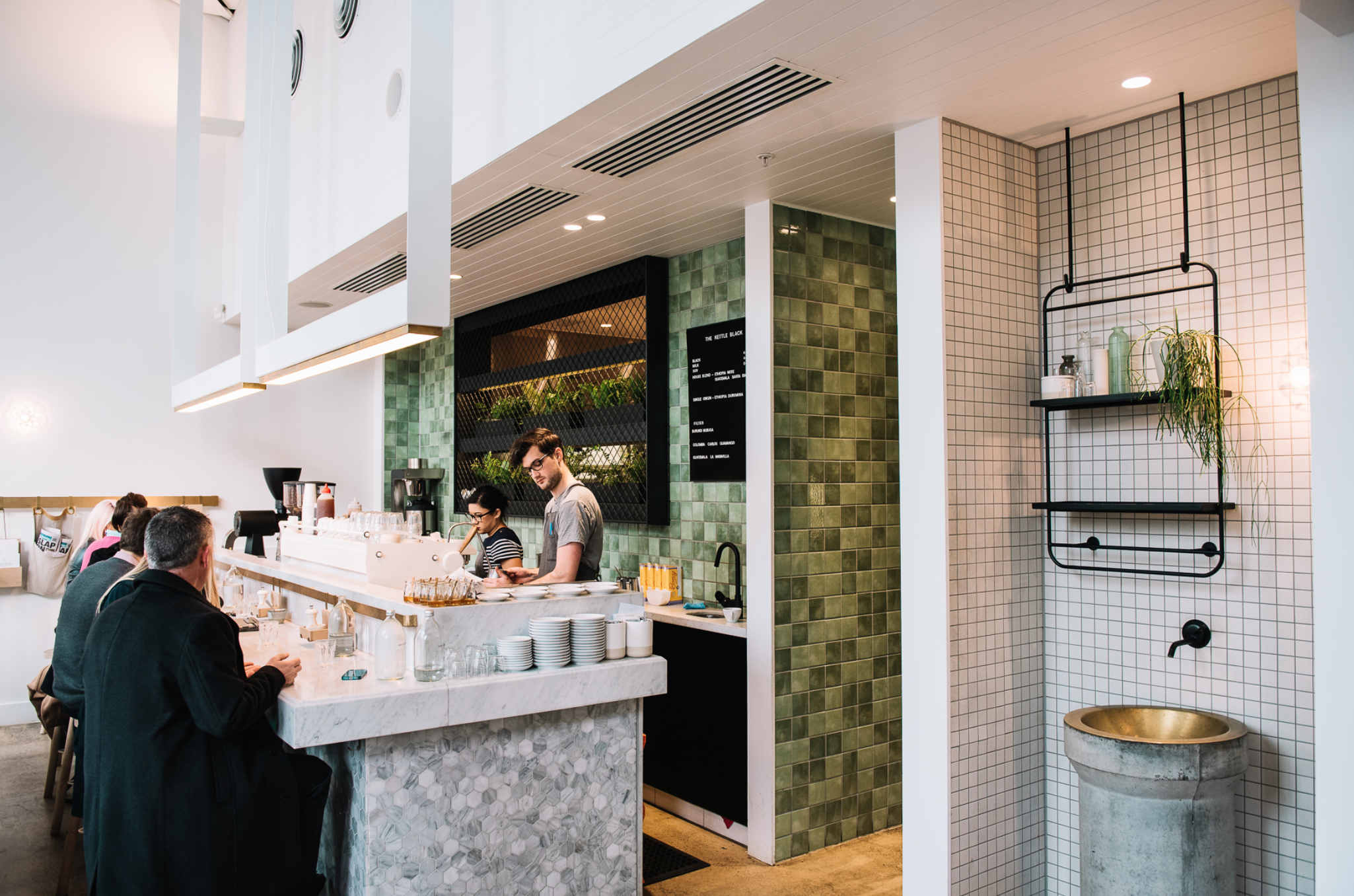 Four people sitting at a coffee bar at Kettle Black, a cafe serving up some of the best breakfast dishes Melbourne has to offer