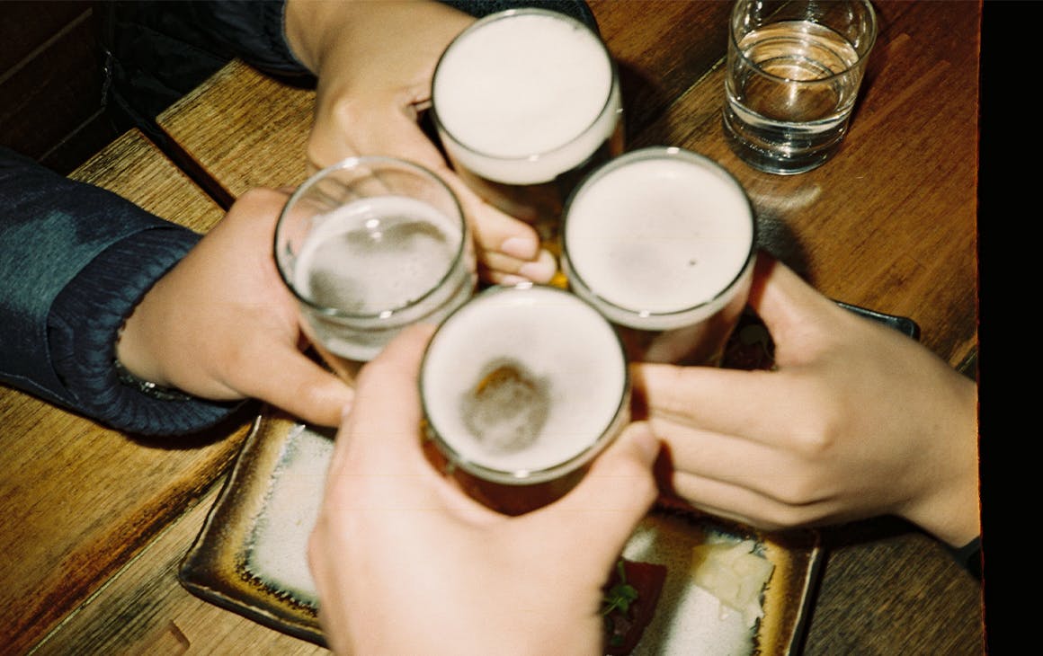 four beer glasses being clinked by different hands