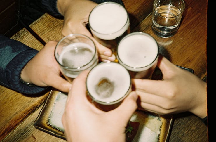 four beer glasses being clinked by different hands