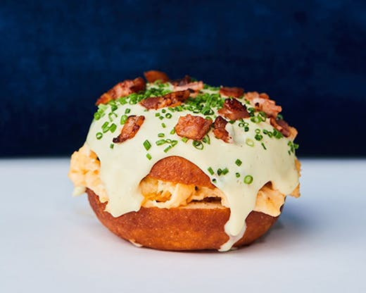 A donut with bacon and eggs stuffed in the middle. A rich hollandaise sauce is dripping from thesides. 
