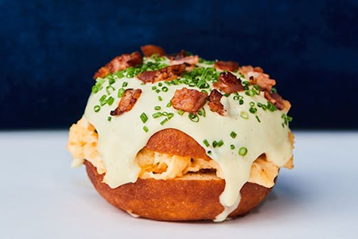 A donut with bacon and eggs stuffed in the middle. A rich hollandaise sauce is dripping from thesides.