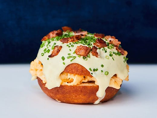 A donut with bacon and eggs stuffed in the middle. A rich hollandaise sauce is dripping from thesides. 
