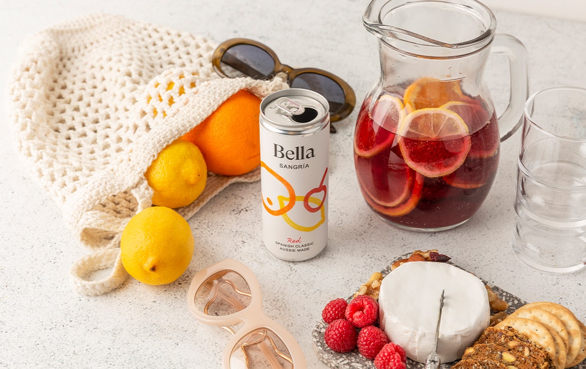 a can of sangria amongst a a bag of lemons, a jug of sangria, and a cheese plate