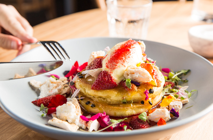 A stack of three pancakes topped with fresh strawberries, edible flowers and passionfruit at Bentwood—a cafe dishing up one of the best breakfasts in Melbourne