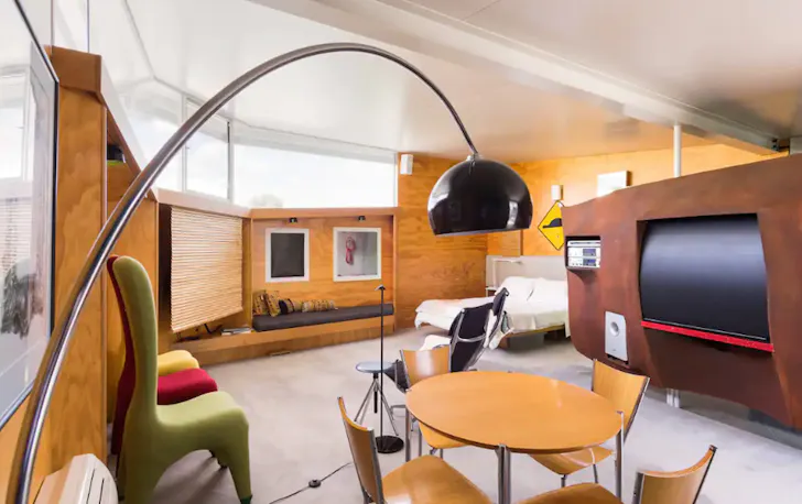 This Airbnb Melbourne living room is almost a circle, with timber walls enclosing the space. A large TV screen sits in an arched TV unit, with three sofa chairs sitting opposite it.