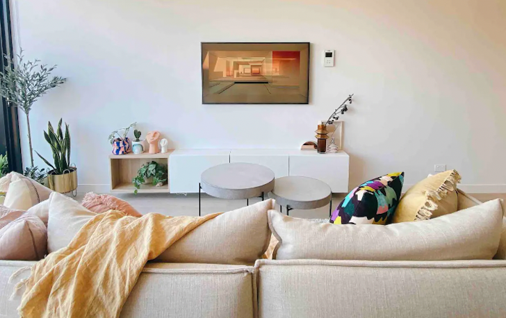 A cream coloured sofa faces a white wall in an Airbnb Melbourne living room with a picture hung on the wall.