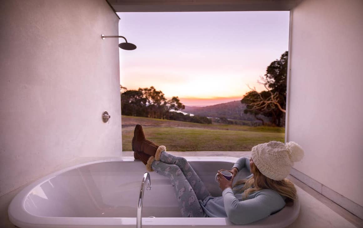 a woman sits in an outdoor bathtub looking out over the countryside
