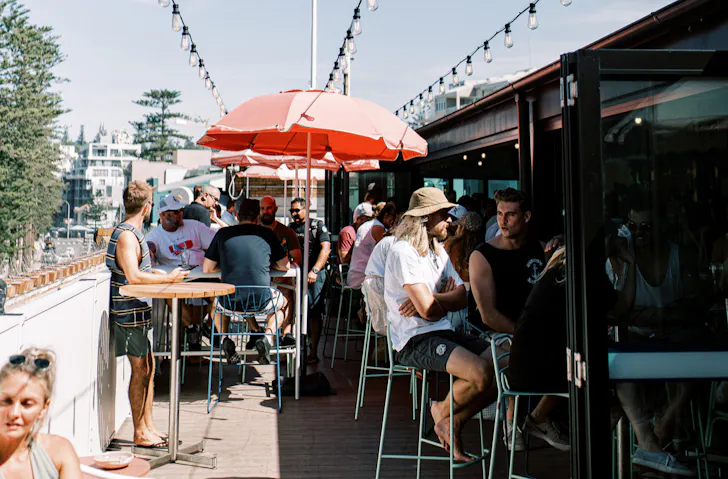 People sit under red beach umbrellas on the rooftop terrace at Hotel Steyne in Manly. 
