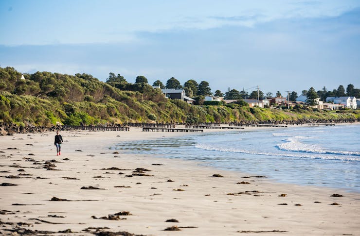 A person walks along the beach at Port Fairy, the town can be seen in the distance.