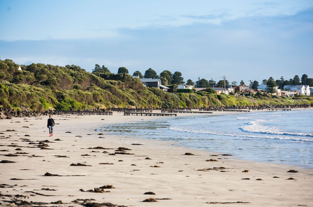 A person walks along the beach at Port Fairy, the town can be seen in the distance.
