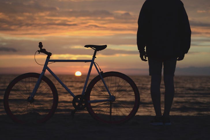 A man standing beside his bike at the seaside at sunrise. 