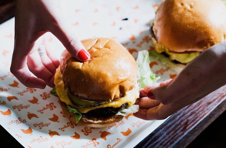 Two hands picking up a juicy burger from Leonard's House of Love, which is considered one of the best burgers in Melbourne. 