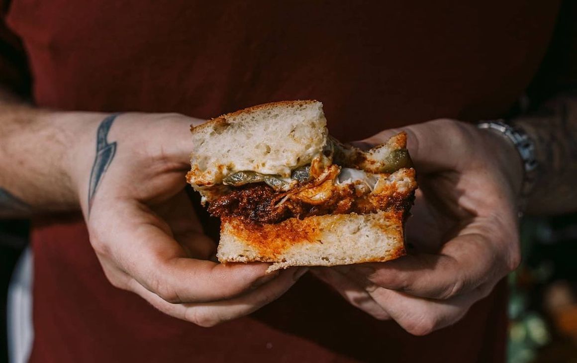 two hands holding a focaccia filled with fried chicken and pickles