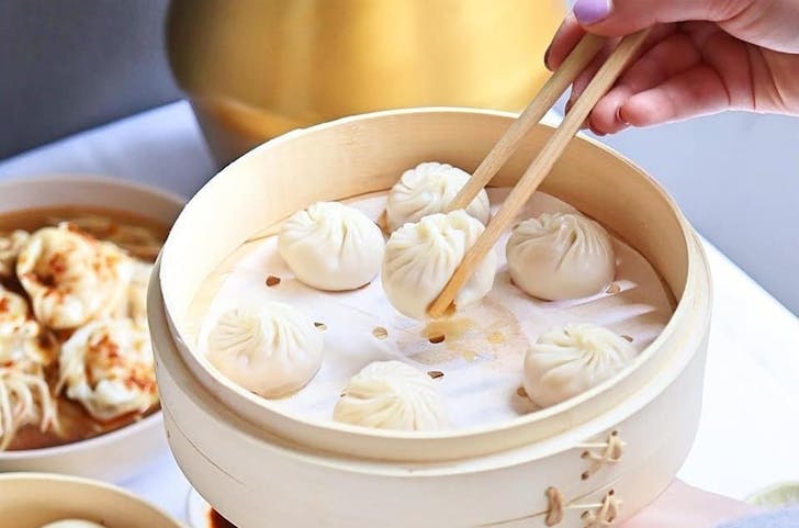 A chopstick reaching into a tray with steamed dumplings at one of the best Chinese restaurants in Melbourne.