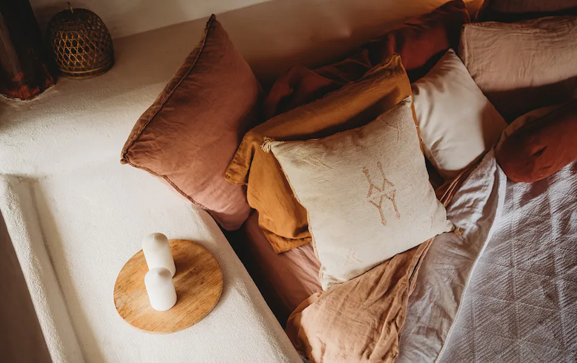 warm orange and beige cushions are artfully arrayed on a bed with a natural stone headboard