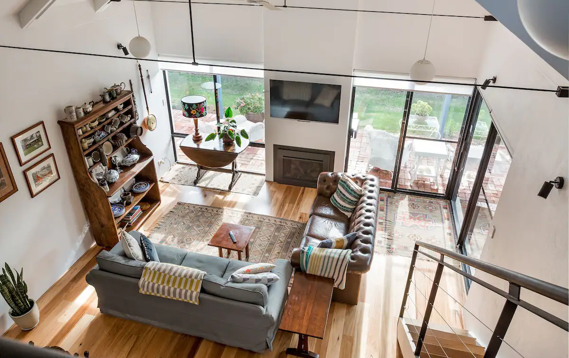 Upstairs view overlooking a living room with comfy leather couches, a fireplace and a shelf with knick-knacks