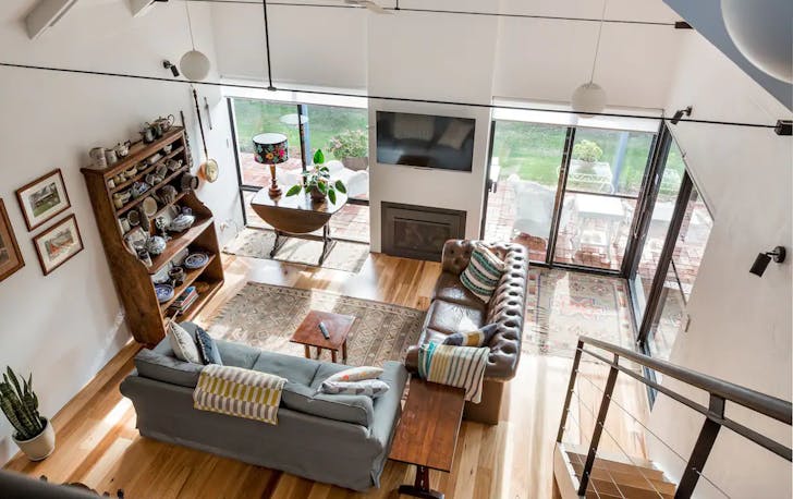 Upstairs view overlooking a living room with comfy leather couches, a fireplace and a shelf with knick-knacks