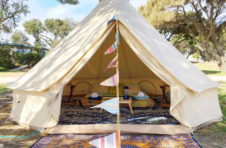 The opening to a glamping tent in Victoria with rugs and a bed set up.
