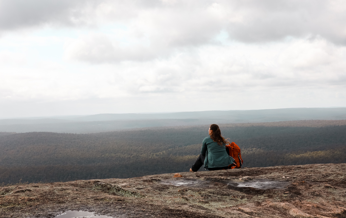 a hiker sitting at the top of Mount Cuthbert looking out over forests