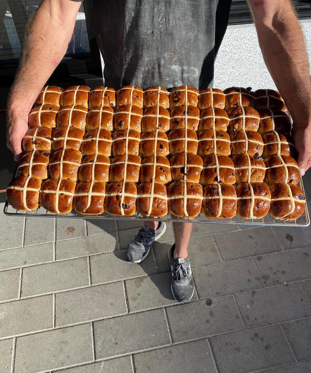 baker holding a rack of hot cross buns