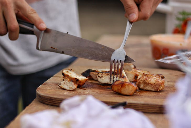 A person cutting chicken with one of the best kitchen knives you can buy.