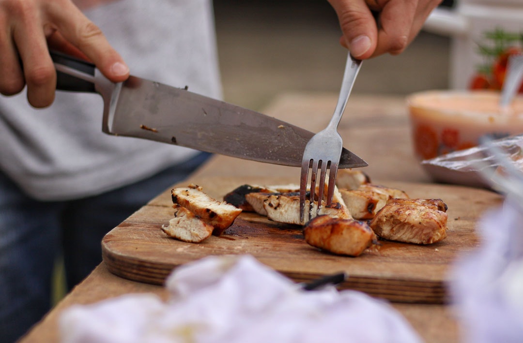 A person cutting chicken with one of the best kitchen knives you can buy.