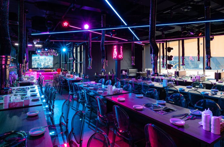 The dining room at BOM Korean BBQ in Sydney, which is drenched in pink and blue neon lights. 