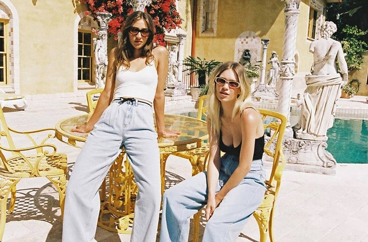Models sitting by a pool wearing wide leg jeans. 