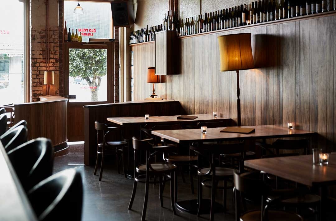 Wooden panelled walls with looming wine bottles above at one of the best wine bar Melbourne has to offer in 2023, Old Palm Liquor.