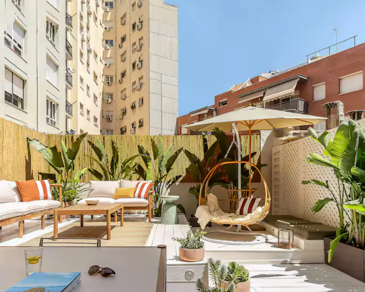 The outdoor terrace of a Barcelona Airbnb, including an egg swinging chair and plenty of greenery.