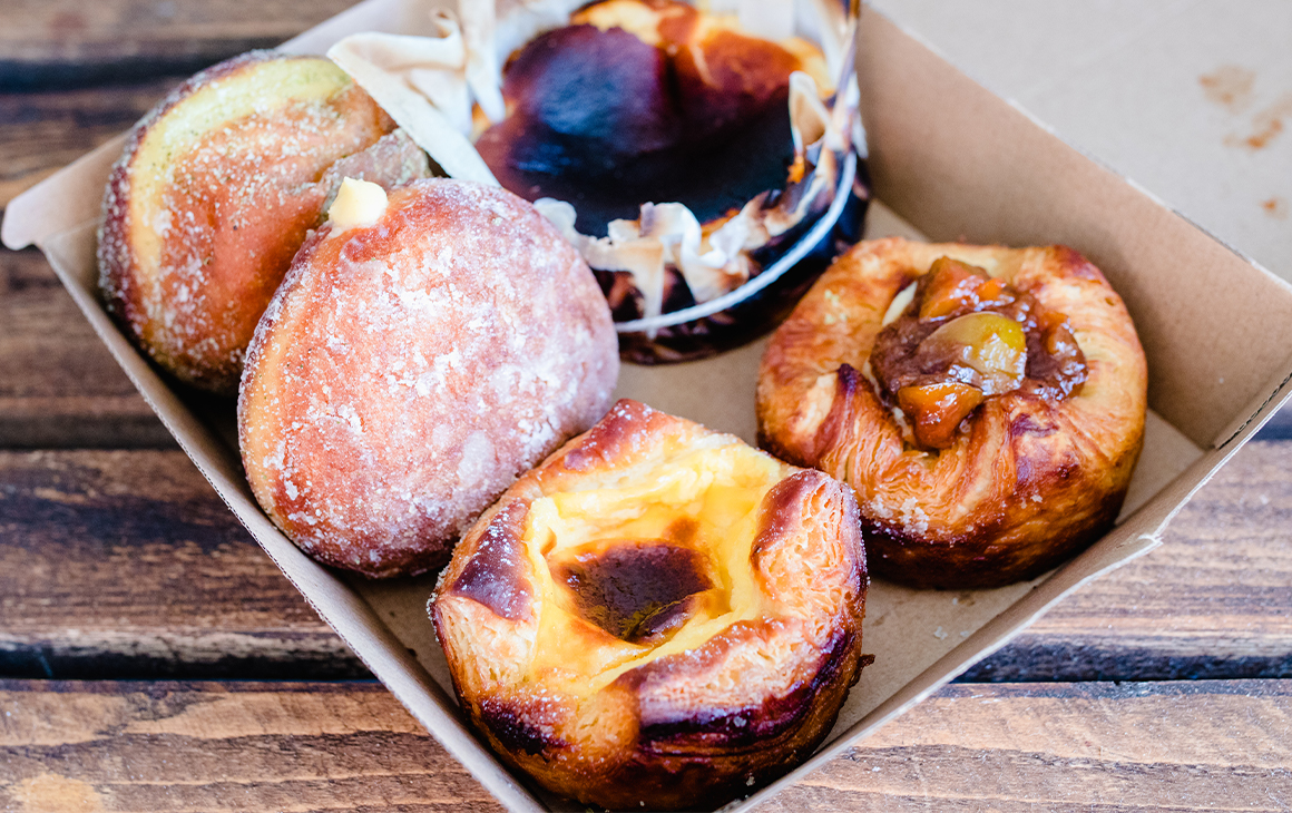 Several pastries including doughnuts, a burnt basque cheesecake and danishes in a cardboard box.
