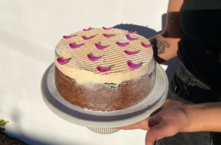 hands holding a cake topped with pink icing and flower petals