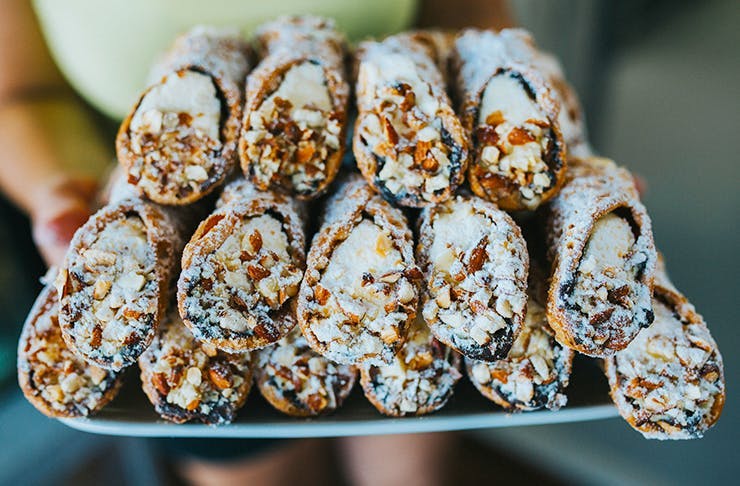 Someone holds a tray, lined with three levels of delicious-looking cannoli. 